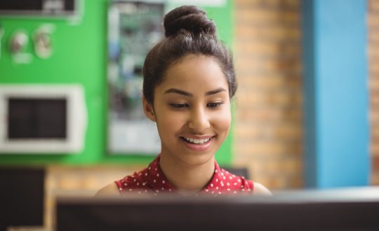 Adolescdente escolar mirando contenta a su computadora