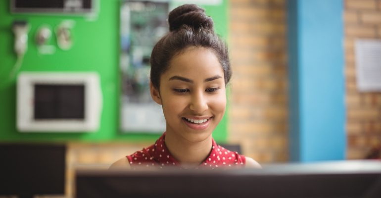 Adolescdente escolar mirando contenta a su computadora